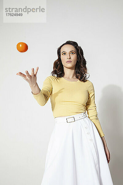 Frau spielt mit Mandarine vor weißem Hintergrund