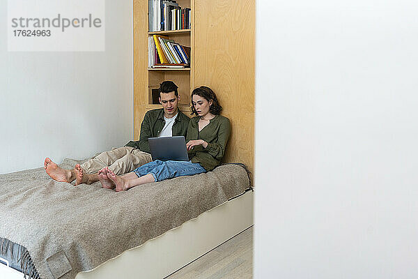 Junges Paar teilt sich Laptop und sitzt zu Hause im Bett