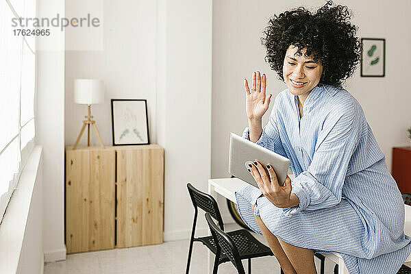 Glückliche Frau winkt bei Videoanruf über Tablet-PC zu Hause mit der Hand