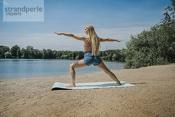 Frau praktiziert am Wochenende Yoga am Seeufer