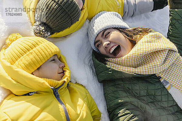 Cheerful mother with sons lying down on snow