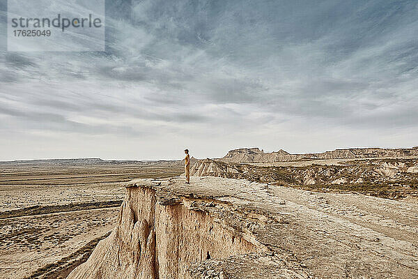 Frau steht auf einer Klippe in der Wüstenlandschaft unter bewölktem Himmel