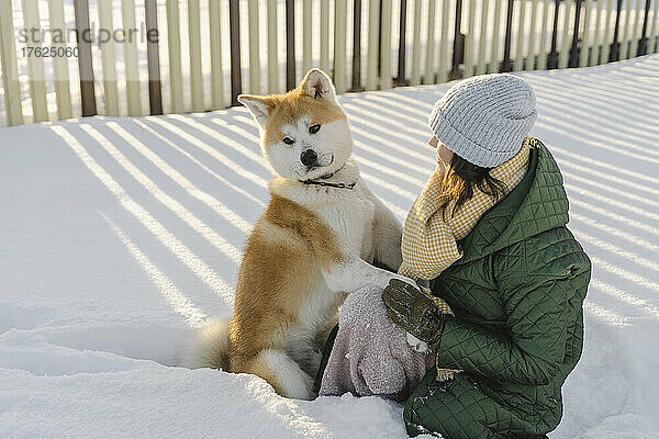 Lächelnde Frau sitzt mit Akita-Hund im verschneiten Garten