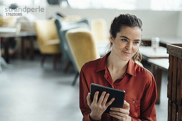 Lächelnde Frau mit Tablet-Computer  die im Café nachdenkt