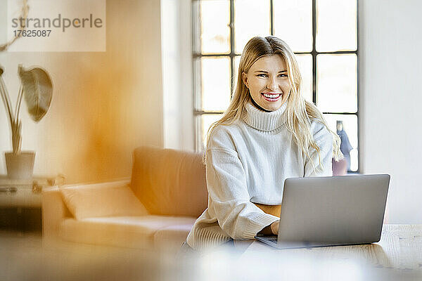 Glückliche Geschäftsfrau mit Laptop  die zu Hause sitzt