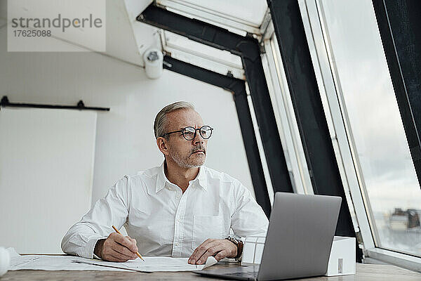 Nachdenklicher Geschäftsmann mit Laptop auf dem Schreibtisch im Büro
