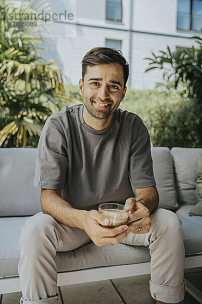 Smiling man holding coffee cup sitting in lounge