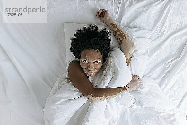 Smiling woman with hand raised lying down on bed at home