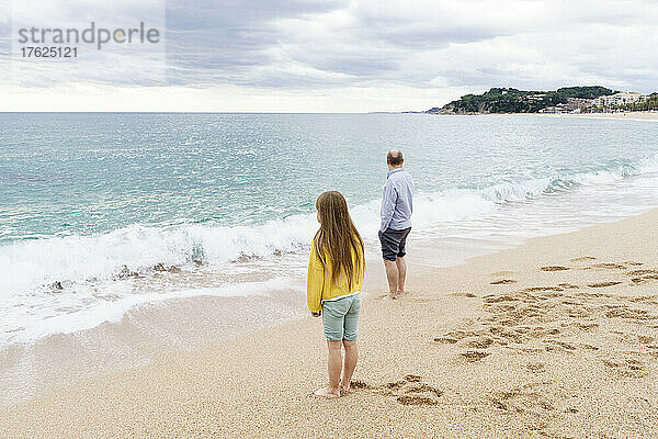 Vater und Tochter stehen an der Küste am Strand