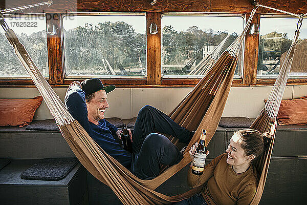 Lächelnde Frau mit Mann  der in der Hängematte auf dem Boot liegt
