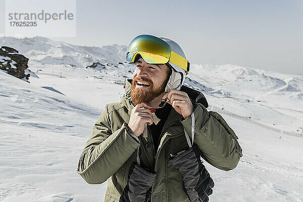 Lächelnder junger Mann mit Bart  der seinen Skihelm befestigt