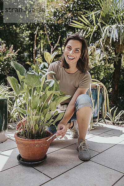 Lächelnder Gärtner kniet neben einer Topfpflanze im Garten