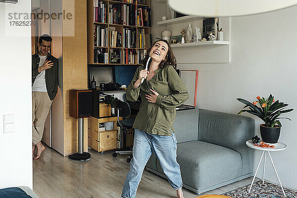 Young man photographing woman singing in living room at home