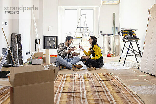Junges Paar isst Essen und sitzt auf dem Boden im neuen Zuhause