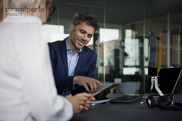 Lächelnder Geschäftsmann diskutiert über Tablet-PC mit Geschäftsfrau im Büro
