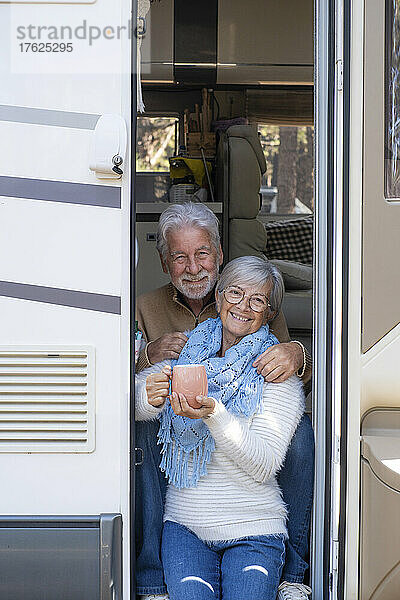 Glückliches älteres Paar mit Kaffeetasse sitzt an der Tür des Wohnmobils