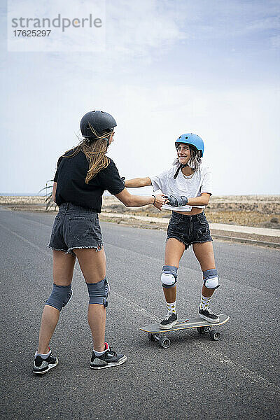 Glückliche junge Frau  die von einer Freundin Skateboarden lernt