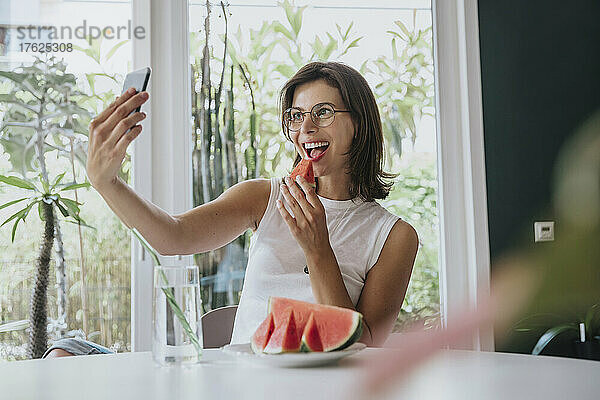 Frau macht ein Selfie und isst Wassermelone  während sie zu Hause sitzt