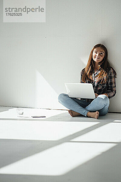 Nachdenkliche Frau mit Laptop vor der Wand zu Hause