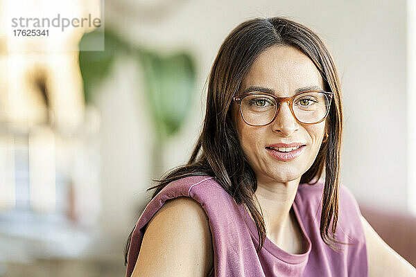 Lächelnde Frau mit braunen Haaren  die zu Hause eine Brille trägt