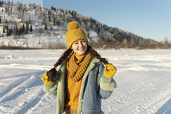 Lächelnde Frau mit Strickmütze steht auf Schnee im Wald