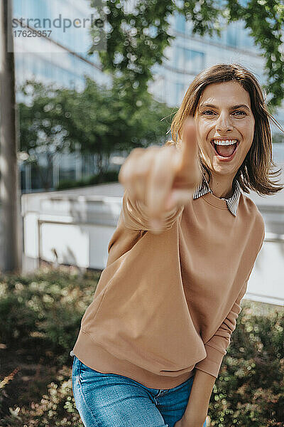 Fröhliche Frau zeigt mit dem Finger im Büropark