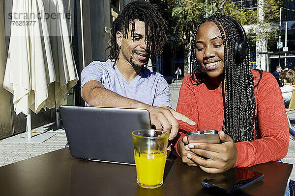 Junger Mann spricht mit Freundin über Smartphone im Straßencafé