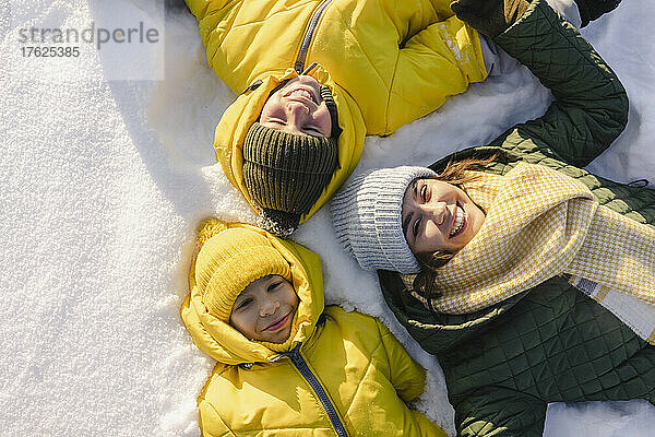 Lächelnde Mutter mit Söhnen  die auf Schnee liegen
