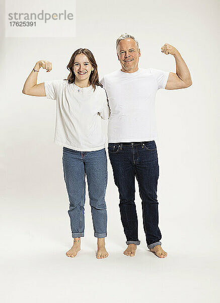 Lächelndes Mädchen mit Vater  der vor weißem Hintergrund Muskeln spielen lässt