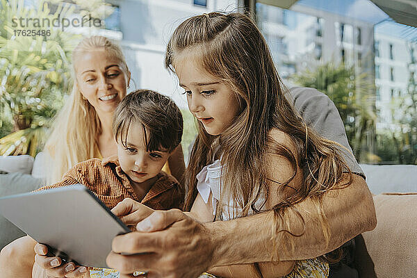 Vater und Kinder nutzen Tablet-Computer auf der Terrasse