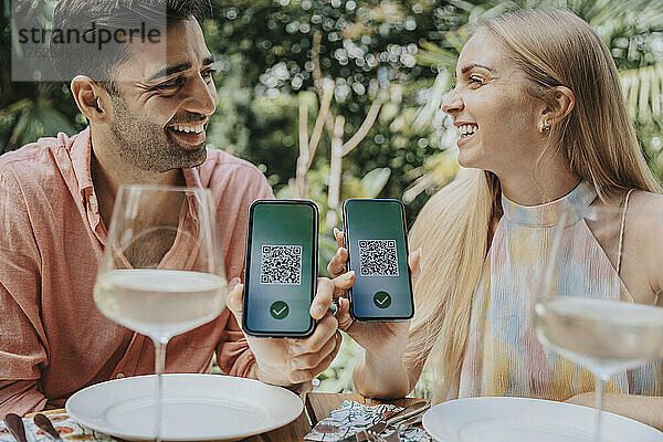 Glückliches Paar zeigt QR-Codes auf Smartphones im Restaurant