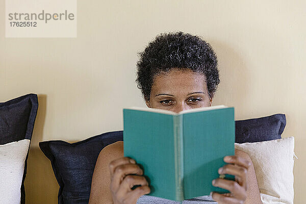 Frau mit schwarzen kurzen Haaren liest zu Hause im Bett ein Buch