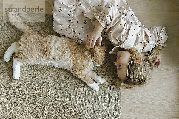 Blondes Mädchen mit Katze liegt zu Hause auf dem Boden