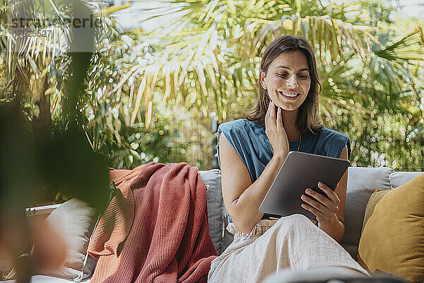Smiling freelancer using tablet PC sitting on sofa in yard