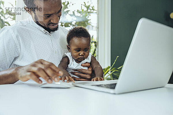 Freiberufler mit Sohn  der im Esszimmer am Laptop arbeitet