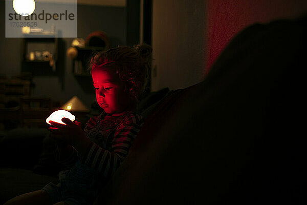 Boy holding illuminated toy in dark room at home