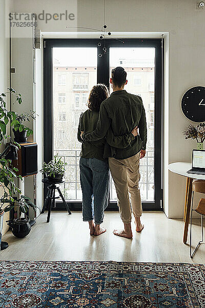 Junges Paar steht zu Hause gemeinsam am Glasfenster