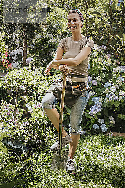 Lächelnder Gärtner steht mit Schaufel im Garten