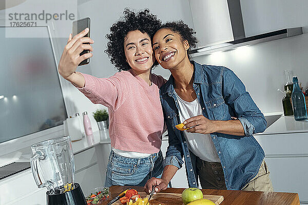Fröhliche Freunde machen ein Selfie mit dem Smartphone  das zu Hause in der Küche steht