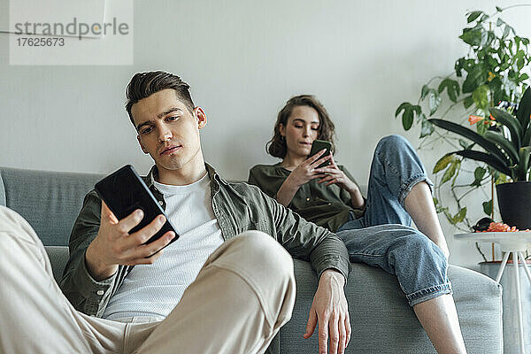 Junges Paar surft im Wohnzimmer über Smartphones im Internet
