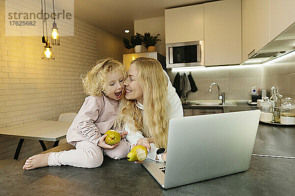 Frau mit Laptop und Birnen von ihrer Tochter in der Küche