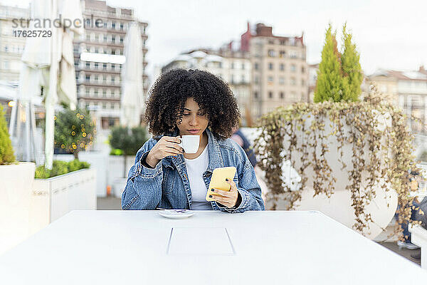 Junge Frau trinkt Kaffee und benutzt Smartphone im Straßencafé