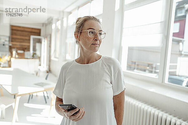 Businesswoman wearing eyeglasses holding smart phone in office