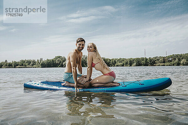 Glückliches Paar sitzt auf einem Paddleboard und schwimmt über dem See