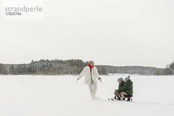 Verspielte Mutter mit Söhnen beim Rodeln im Schnee