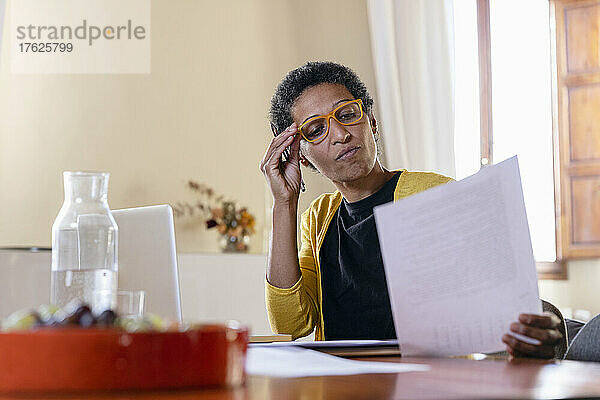 Geschäftsfrau mit Brille prüft zu Hause Papierdokument