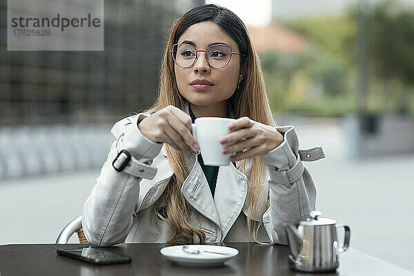 Schöne Frau mit Kaffeetasse sitzt im Straßencafé