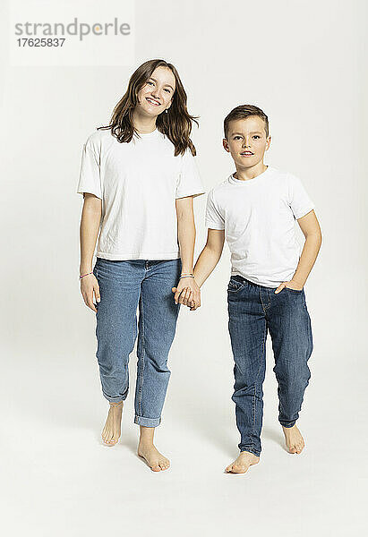 Girl holding brother's hand walking against white background