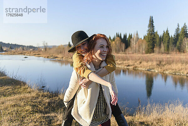 Happy woman carrying her friend piggyback by river