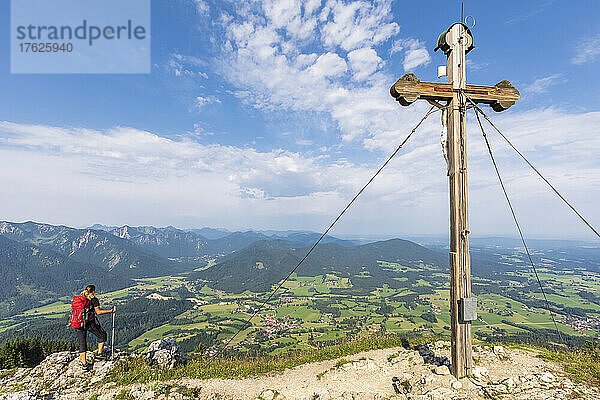 Wanderin bewundert die Aussicht vom Bockstein mit Gipfelkreuz im Vordergrund